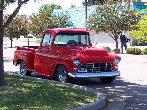 1972 Ford Ranchero - A bright red pickup truck is parked on the side of the road near a building.