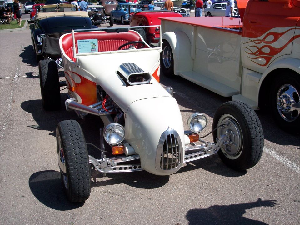 White hot rod roadster with orange flames, chrome grille, and scoop. Other vehicles visible behind