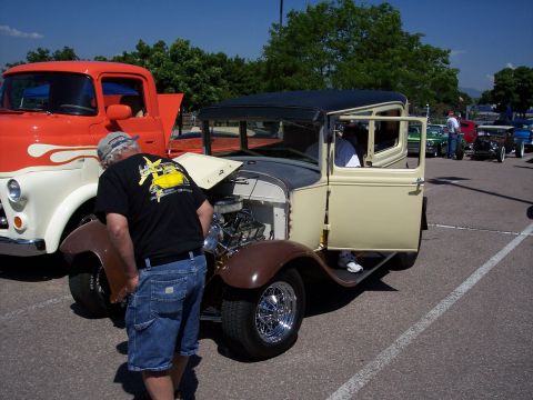 1972 Ford Ranchero - A man examines a tan and brown sedan with its hood up and door open, parked next to an orange and white truck.