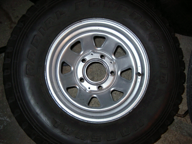 Close-up of a silver multi-spoke wheel with a black tire. Text on tire is partially visible