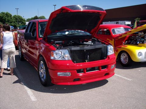 1972 Ford Ranchero - A red pickup truck is displayed with its hood open, parked next to a vintage car at an outdoor event.