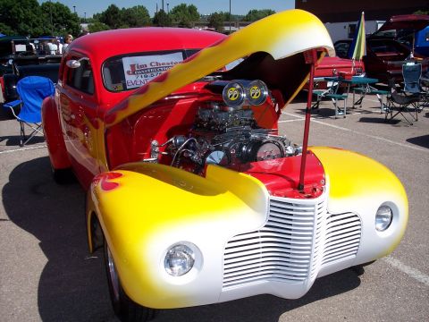 1972 Ford Ranchero - A custom hot rod with a prominent engine and flame paint job is displayed at an outdoor event.