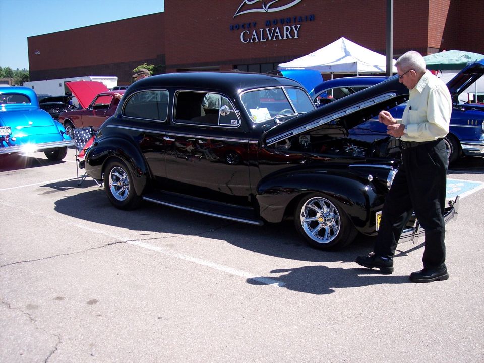Black sedan with hood open, chrome wheels, parked at car show