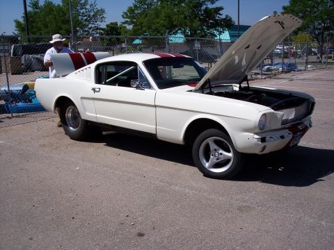 1972 Ford Ranchero - A man stands by a white 1965 Ford Mustang coupe with red racing stripes, its hood open, parked outdoors.