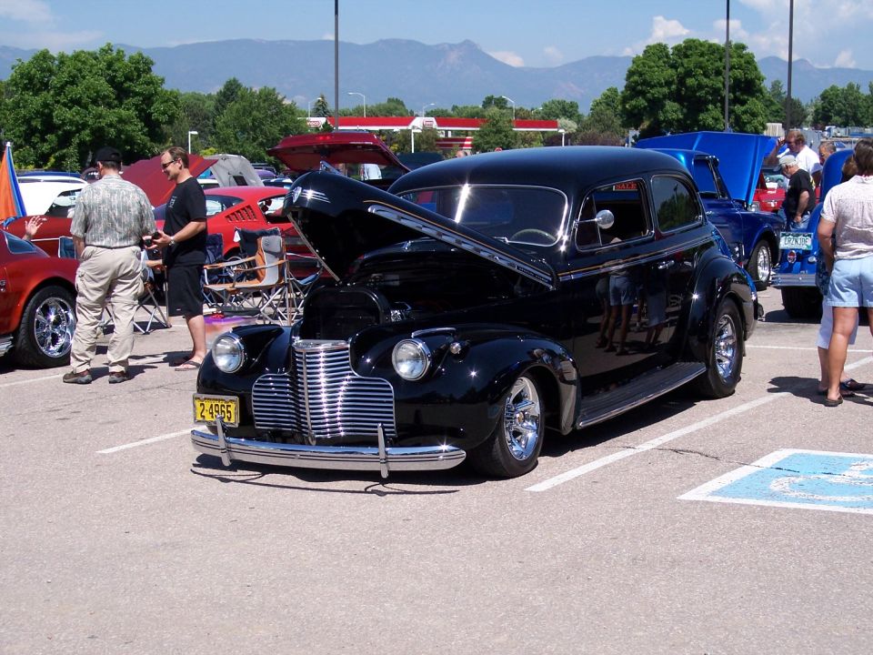 Black vintage sedan with chrome grille and open hood parked at an outdoor event