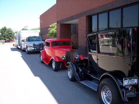 1972 Ford Ranchero - A silver pickup truck, a red hot rod, and a black vintage car are parked in a line outside a brick building.