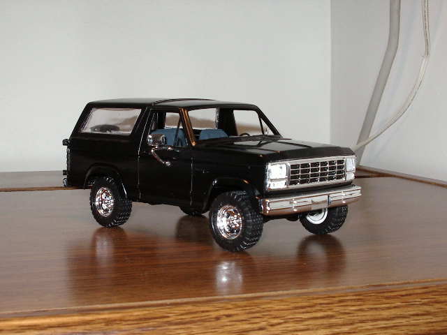 Black Ford Bronco model on wooden surface, 3/4 front view, showing chrome grille and interior