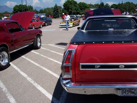 1972 Ford Ranchero - A red pickup truck is parked in a lot with other vehicles, showing its rear end and a black tonneau cover.