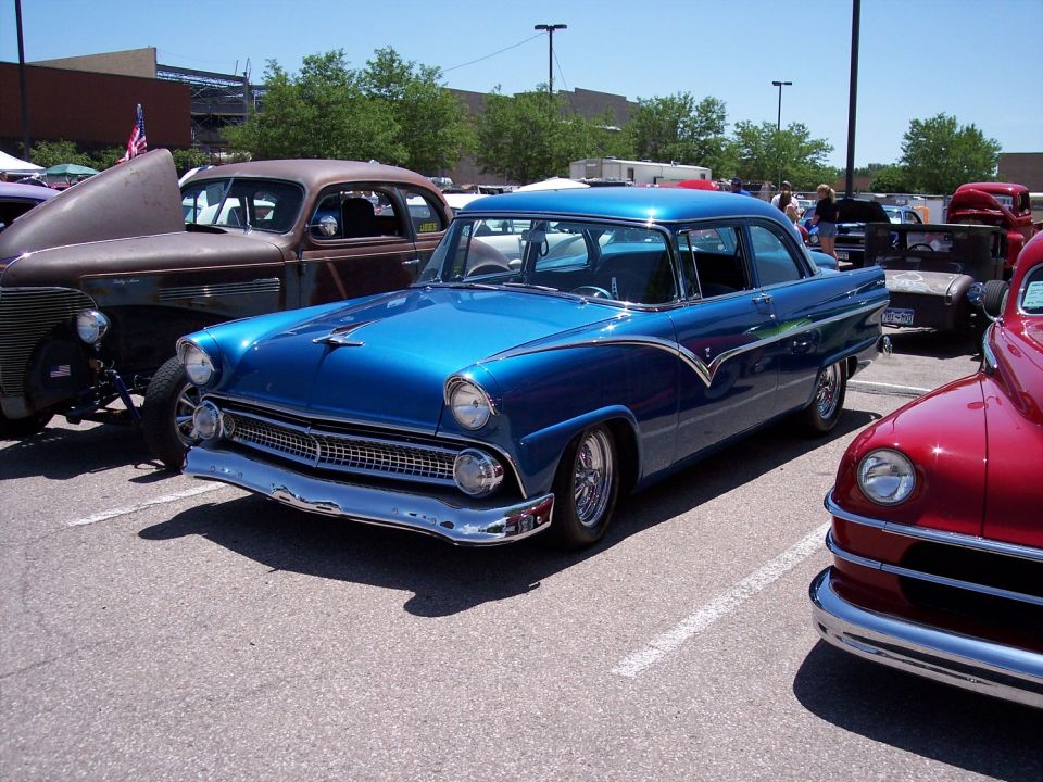 Blue classic sedan parked next to a rusty hot rod and a red classic car