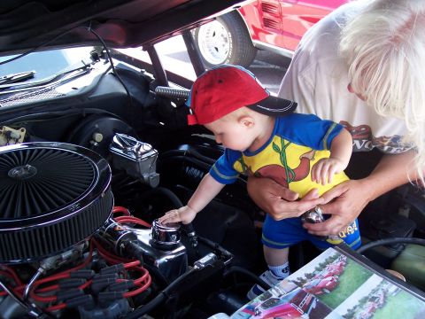 1972 Ford Ranchero - A baby explores the engine compartment of a car, with another vehicle in the background.