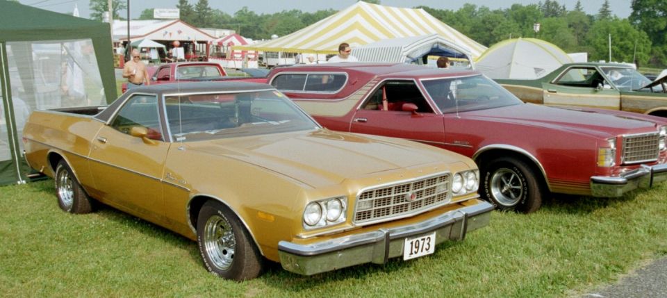 Gold 1973 Ford Ranchero with a black vinyl top, parked on grass