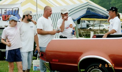 1976 Ford Ranchero - Several people are gathered near the back of an orange vehicle at an outdoor event.