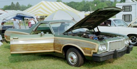 1976 Ford Ranchero - A green pickup truck with wood paneling is displayed with its hood and door open at an outdoor event.