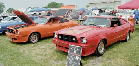 1976 Ford Ranchero - Two Ford Mustang IIs are displayed on a grassy field with tents in the background.