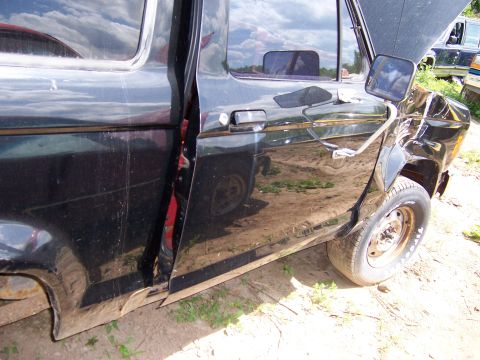 1980 Jeep CJ5 - Side view of a damaged black pickup truck door and fender, with another vehicle in the background.