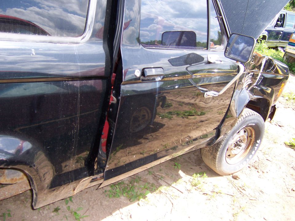 Black pickup truck door and fender with damage. Another vehicle is visible in the background