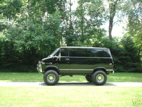 1978 Ford E250 - A black van is parked outdoors on a paved surface with a grassy area and trees behind it.