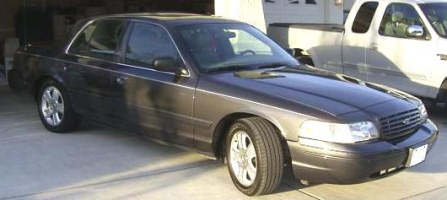 2005 Ford Crown Victoria - A 2005 Ford Crown Victoria is parked in front of a garage, with a white pickup truck beside it.