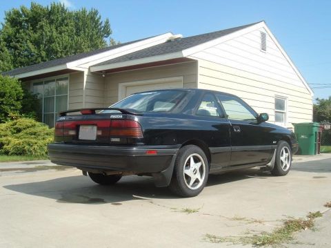 1989 Mazda MX-6 - A black 1989 Mazda MX-6 is parked in a driveway in front of a house.