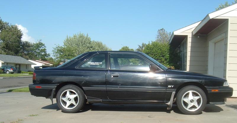 Black coupe parked in front of a house. It has a 'GT' badge on the fender