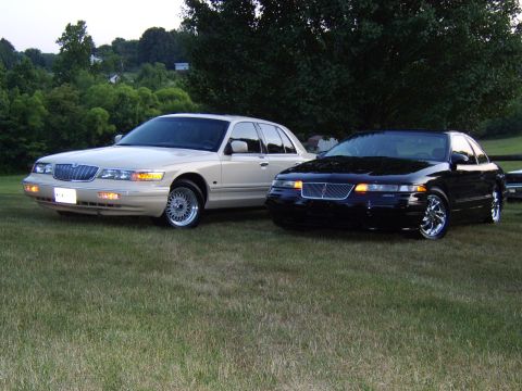 1996 Mercury Grand Marquis - Two sedans, a cream 1996 Mercury Grand Marquis and a black sedan, are parked on a grassy lawn.