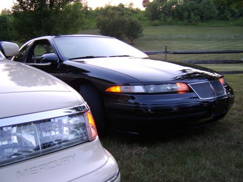 1996 Mercury Grand Marquis - Two cars are parked on a grassy area with a wooden fence in the background.