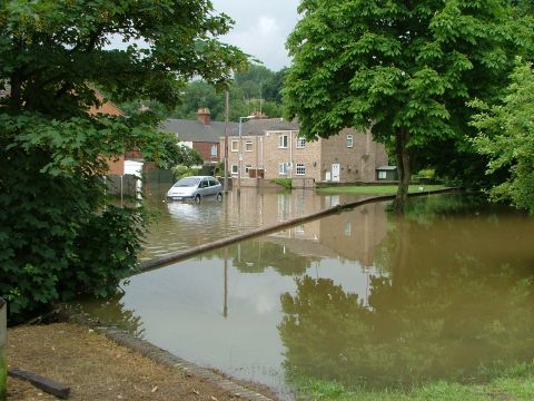 2001 Ford Fiesta - A silver hatchback is submerged in floodwaters on a residential street, with houses in the background.