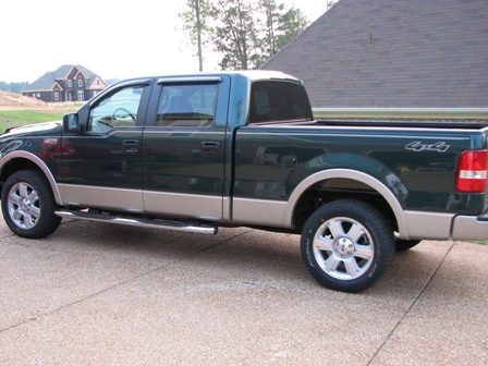 1991 Ford Bronco - This pickup truck is a dark green and tan two-tone model with chrome side steps and 4x4 badging on the rear fender.