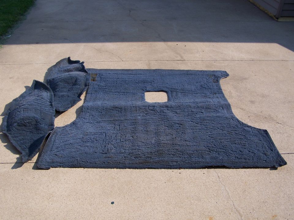 Gray automotive carpet laid out to dry on a concrete driveway
