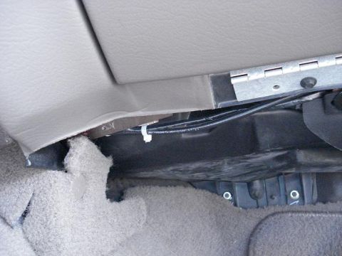 1999 Ford Crown Victoria - Under-dash view on the passenger side with the tan trim panel partly pulled away, exposing a bare metal bracket, a black wiring harness wit…