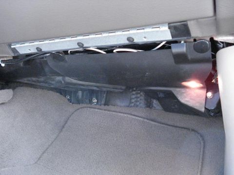 1999 Ford Crown Victoria - Passenger footwell of a car with the lower dash hush panel removed, exposing black HVAC ducting, a bare metal reinforcement bracket and rou…