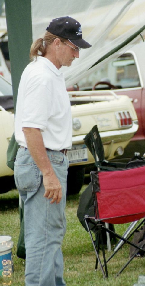 1976 Ford Ranchero - A man wearing a Ford hat stands in front of a classic Ford Mustang convertible at an outdoor event.