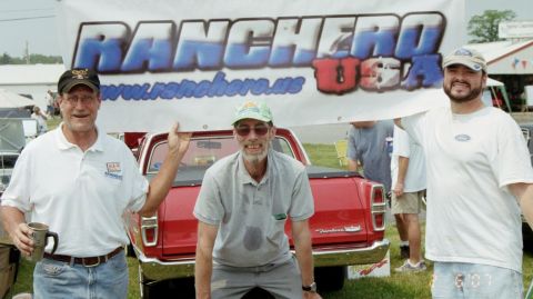 1976 Ford Ranchero - Three men pose for a photo while holding a banner at an outdoor event.
