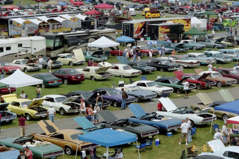 Gold 1972 Ford Gran Torino Sport convertible with black stripes, hood open, parked on grass at a car show
