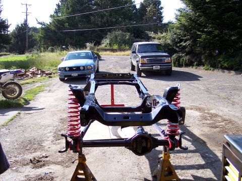 1977 Ford F-150 - A vehicle frame is elevated on jack stands, with other vehicles visible in the background.