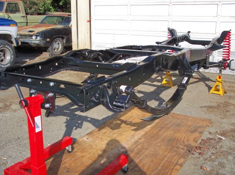 1977 Ford F-150 - A disassembled truck frame is supported by stands, with other vehicles visible in the background.