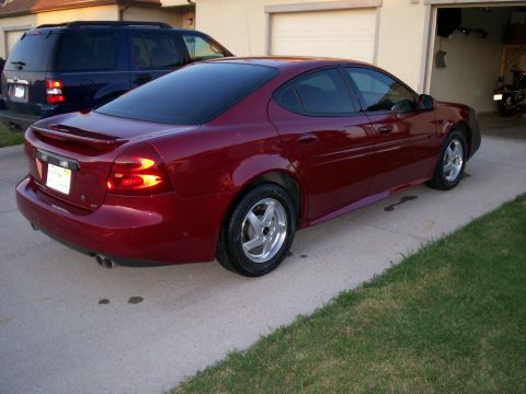 2004 Pontiac Grand Prix - A red 2004 Pontiac Grand Prix is parked in a driveway with a dark SUV behind it.