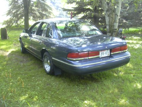 1996 Ford Crown Victoria - A dark blue 1996 Ford Crown Victoria is parked on a grassy area, seen from the rear with its license plate visible.