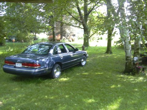 1996 Ford Crown Victoria - A blue 1996 Ford Crown Victoria is parked on a lawn surrounded by trees.
