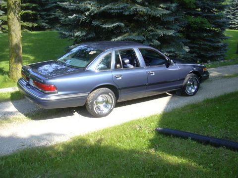 1996 Ford Crown Victoria - A blue Ford Crown Victoria is parked on a gravel driveway with a grassy area and trees in the background.