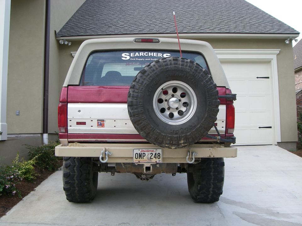 Rear of lifted red and tan Ford Bronco with Super Swamper spare on swing-out tire carrier