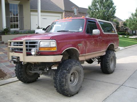 1995 Ford Bronco - A lifted red Ford Bronco with a tan lower two-tone and tan top parked in a residential driveway, wearing a tan brush guard with winch and d…