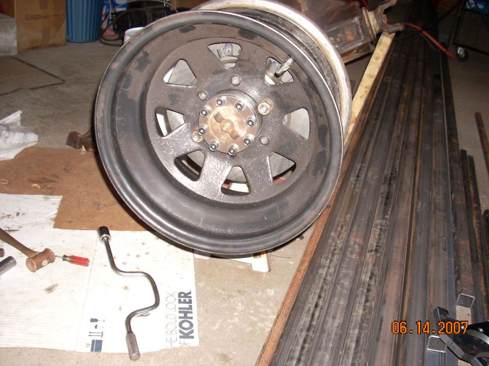 Rusty 6-lug wheel with a chrome center cap, resting on a concrete floor next to metal bars