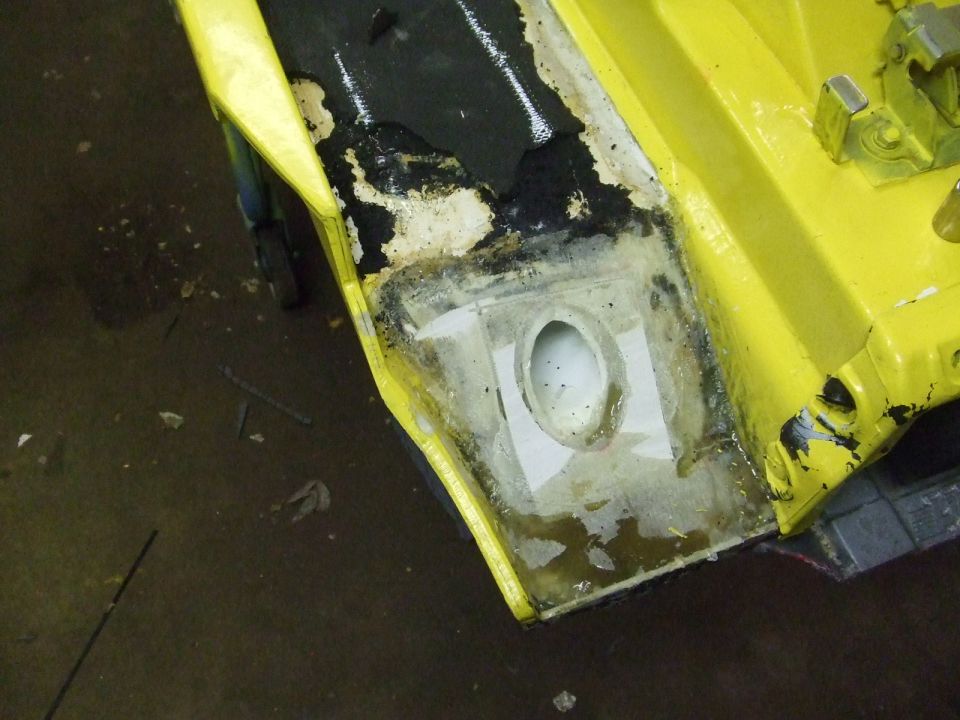Close-up of yellow car body panel with damaged area being repaired, showing exposed metal and filler