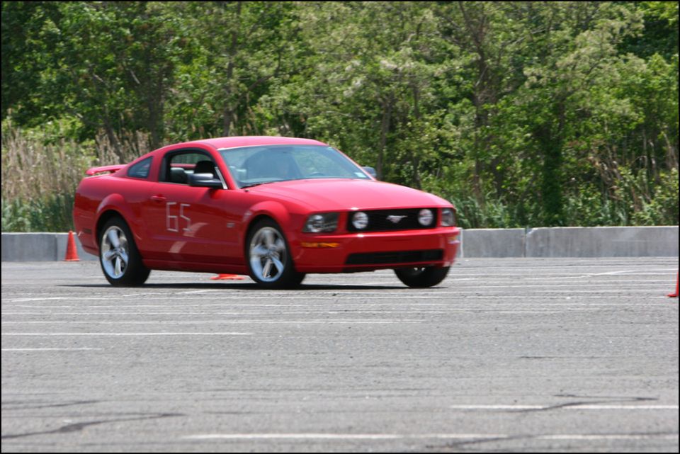 Red Ford Mustang with number 65 on the side, driving on a paved track