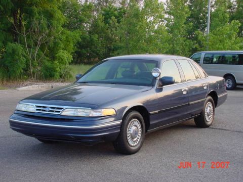 2003 Ford Crown Victoria - A blue 2003 Ford Crown Victoria, likely a police interceptor, is parked outdoors with a spotlight visible.