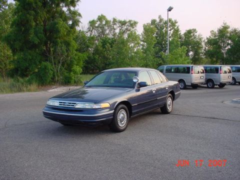 2003 Ford Crown Victoria - A 2003 Ford Crown Victoria police car is parked outside, with several vans visible in the background.