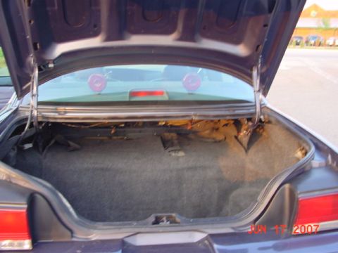 2003 Ford Crown Victoria - The trunk of a sedan is open, revealing the cargo area and the rear window with two circular red lights.