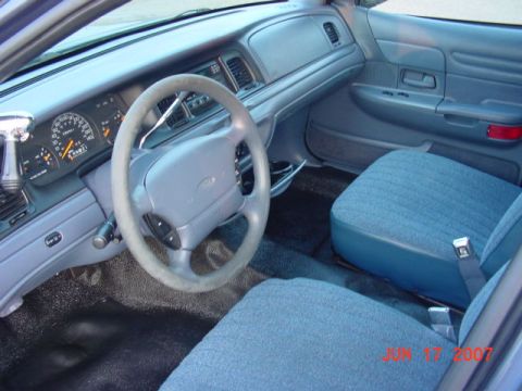 2003 Ford Crown Victoria - The interior of a 2003 Ford Crown Victoria shows blue cloth seats and a dashboard with a steering wheel.
