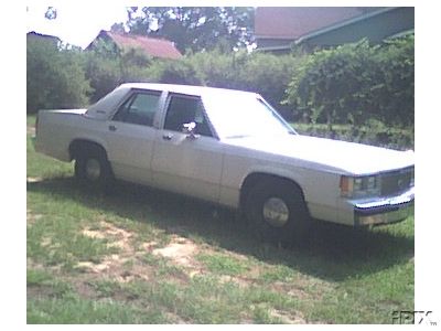 1991 Ford Crown Victoria - This 1980s Ford sedan is parked on a grassy area with trees and houses in the background.